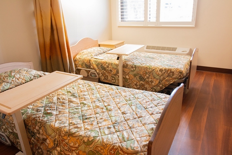 Resident Room - Our semi private rooms are equipped with privacy curtains, long-term care beds (e.g., adjustable height & positioning), over-bed trays, an AC unit, and a window overlooking the facility's lush environment.